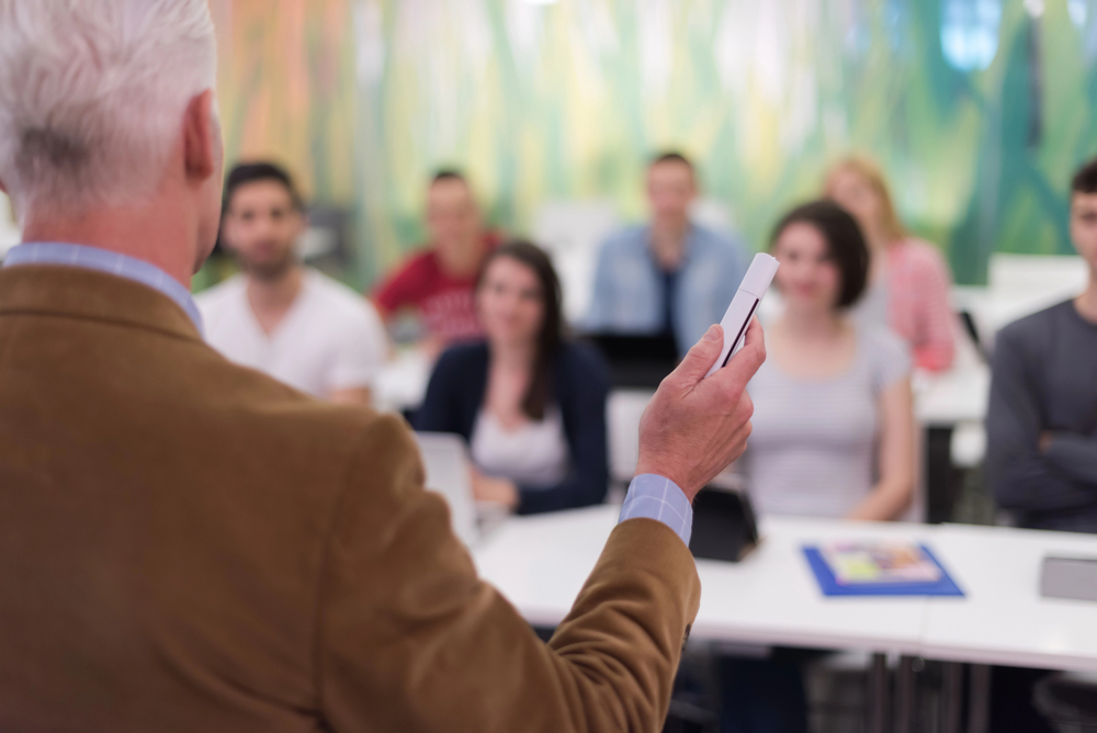 Grafika przedstawia ludzi siedzących w sali konferencyjnej