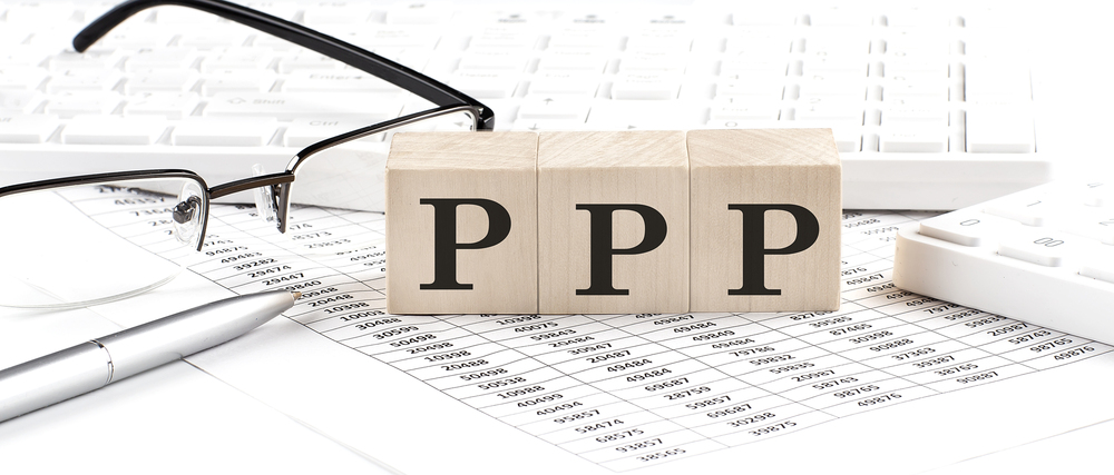 Na zdjęciu widoczny fragment klawiatury laptopa, okulary, fragment dokumentu i trzy drewniane klocki ułożone obok siebie. Na każdym klocku litera P. Litery tworzą napis PPP.