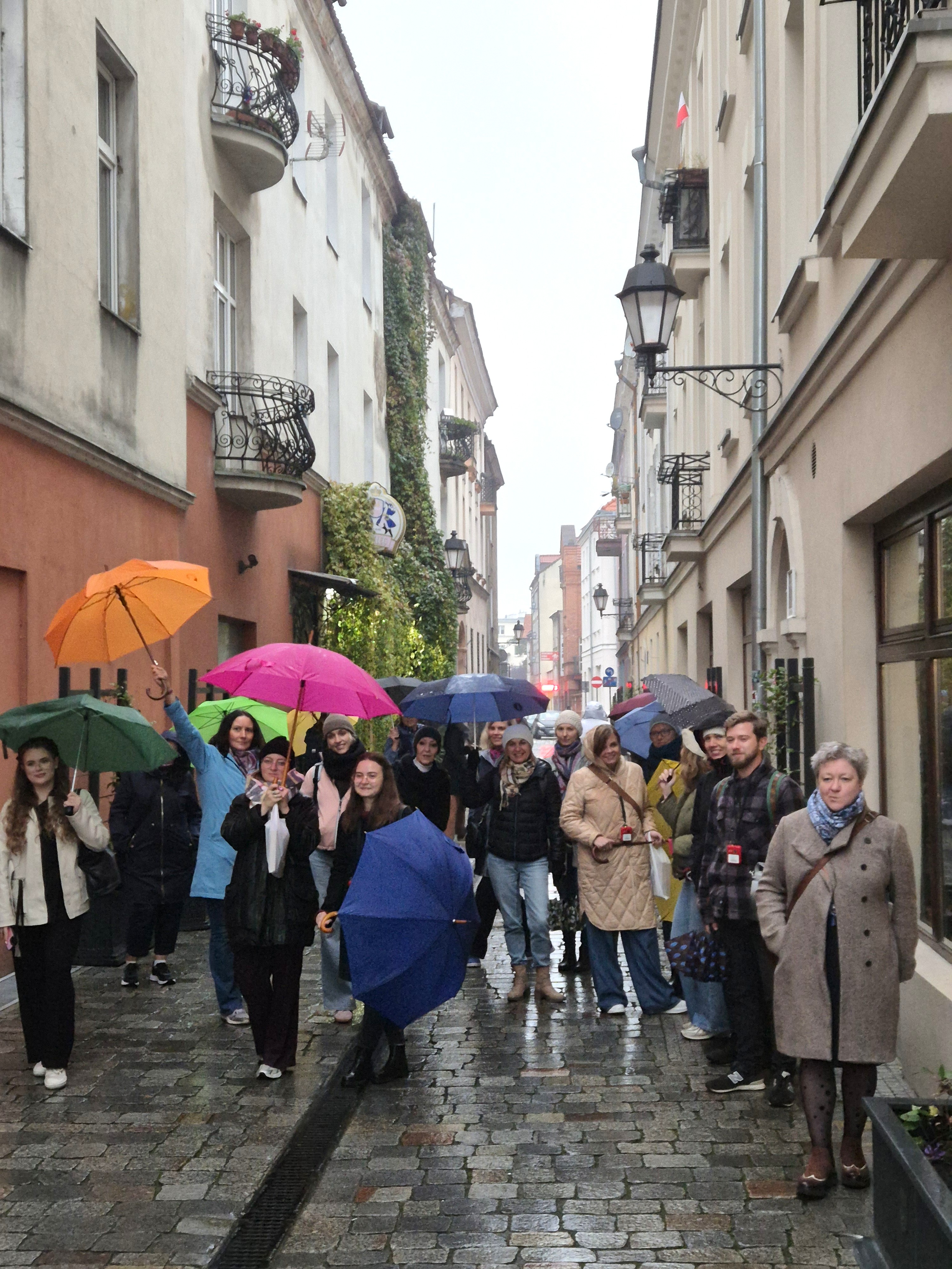 Grupa ludzi z parasolami w wąskiej uliczce