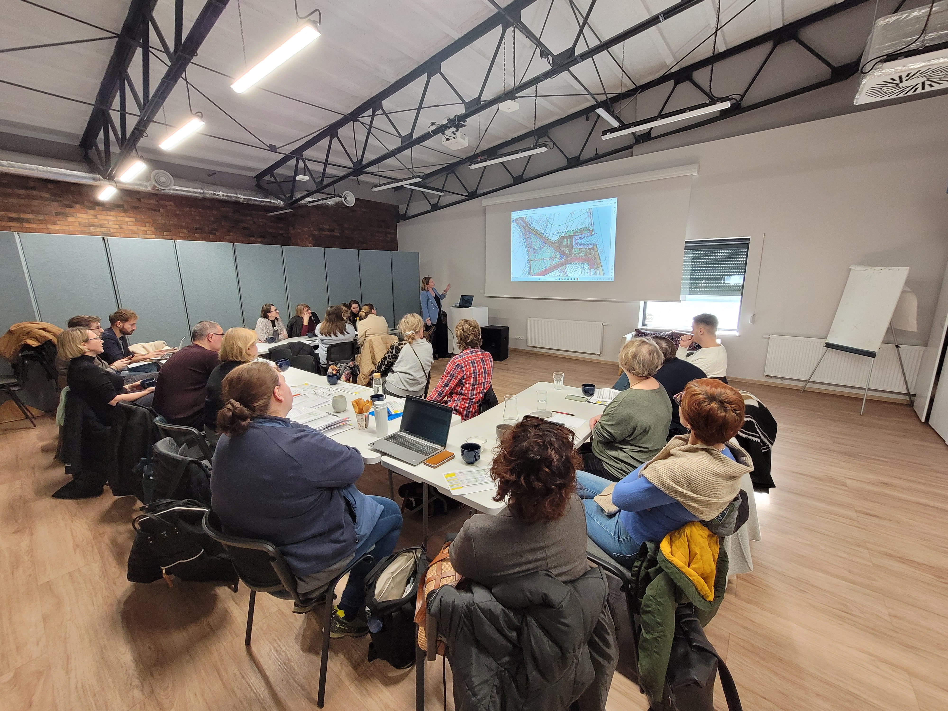 Grupa ludzi siedząca przy stole i oglądająca prezentację