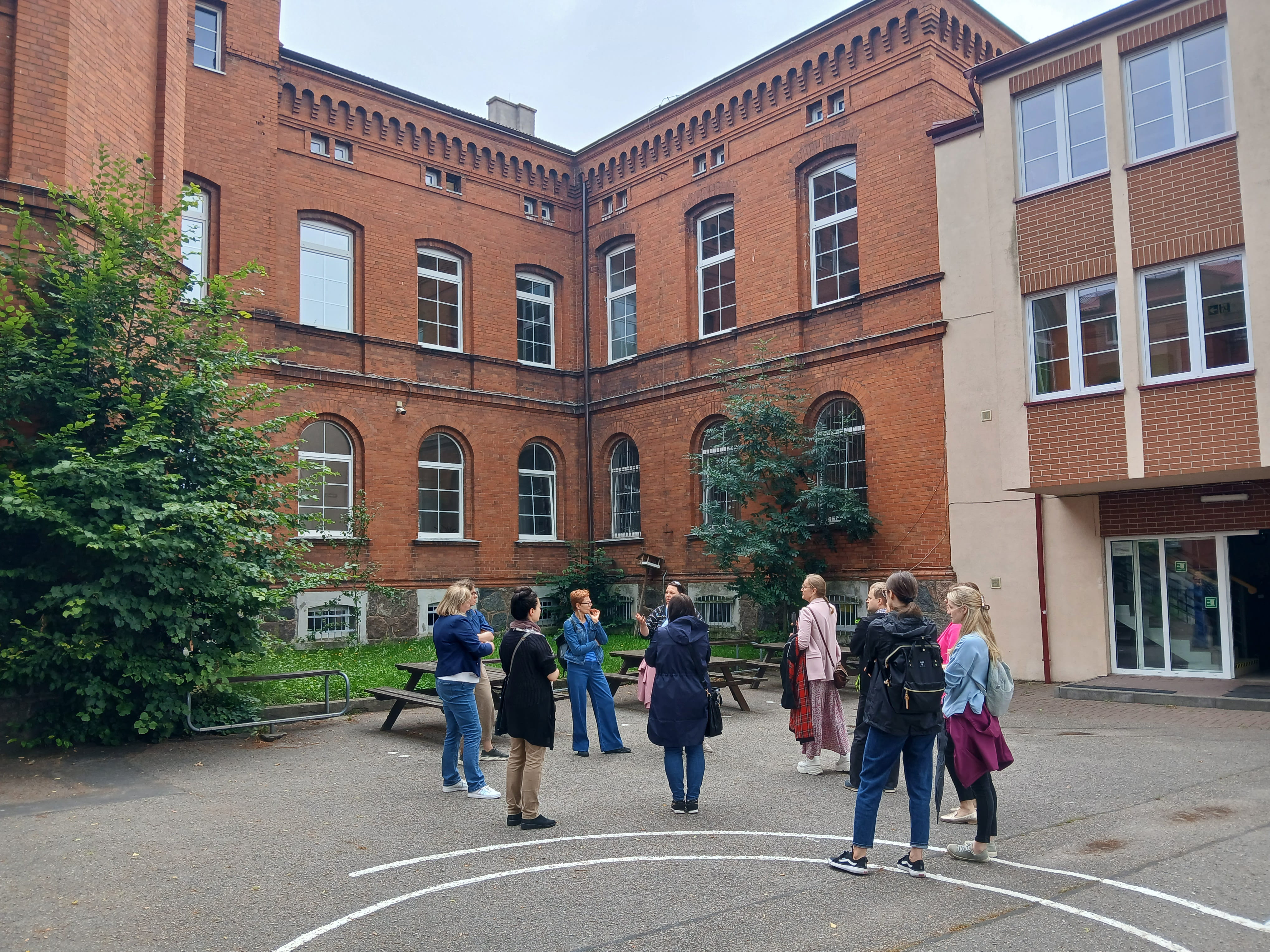 Grupa ludzi stojąca pod wysokim budynkiem z czerwonej cegły
