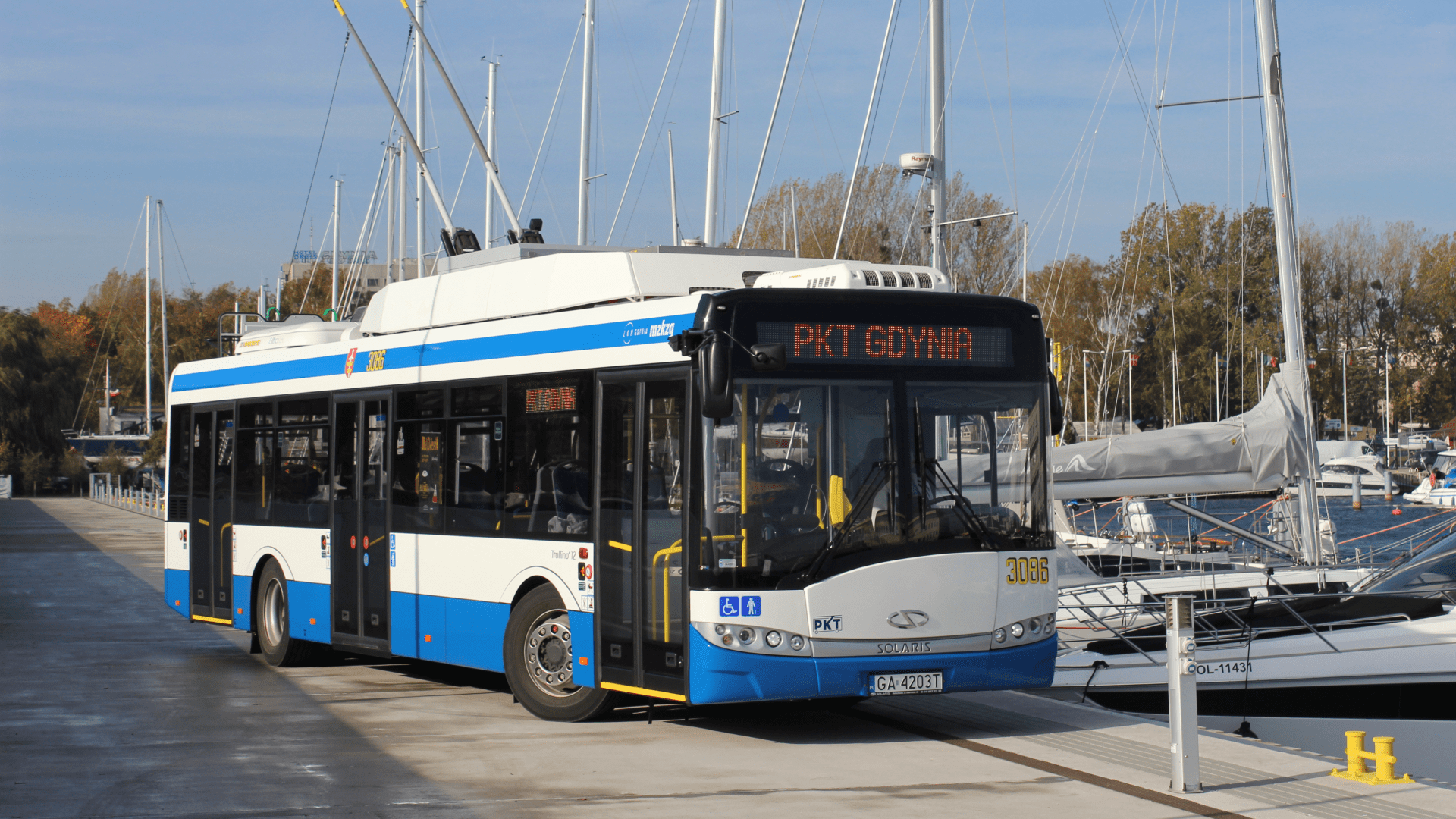 Biało-niebieski autobus na tle łodzi żeglarskich