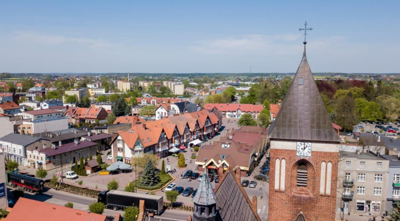 a zdjęciu widać centrum małego miasta widziane z lotu ptaka. Na pierwszym planie widoczna jest wieża widokowa z zegarem, a w tle niskie zespoły budynków z dwuspadowymi dachami.