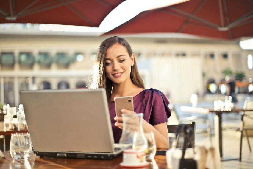 Kobieta korzysta z telefonu. Przed nią stoi laptop