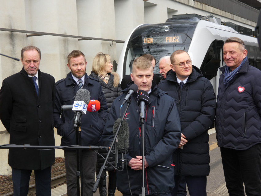 Grupa ludzi, wśród których jest marszałek Mieczysław Struk oraz wicemarszałek Leszek Bonna. Na pierwszym planie mikrofon, w tle pociąg