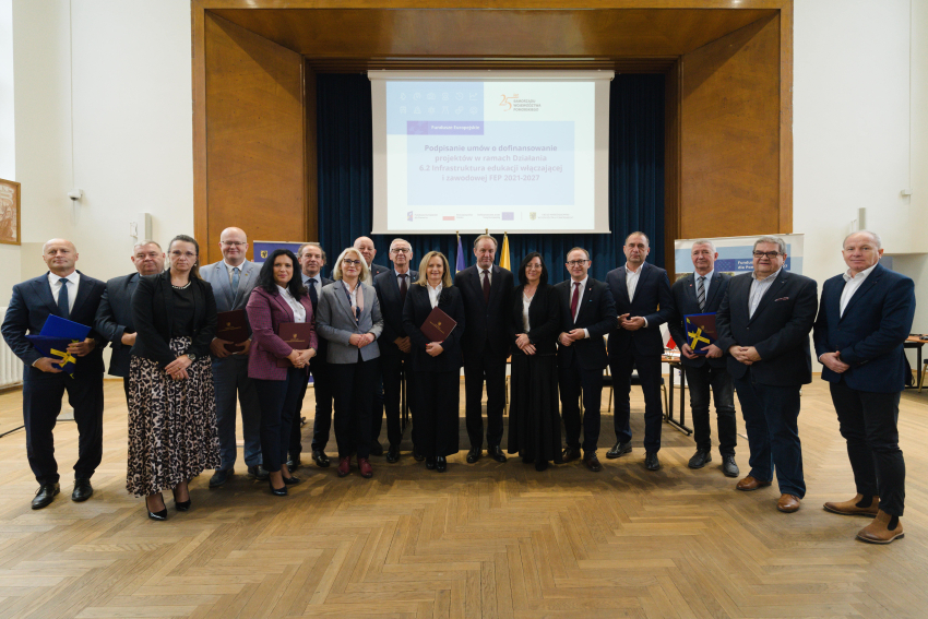 Zdjęcie grupowe siedemnastu osób w tym marszałek Mieczysław Struk, wicemarszałek Marcin Skwierawski prezentują podpisane umowy oraz flagi unijne