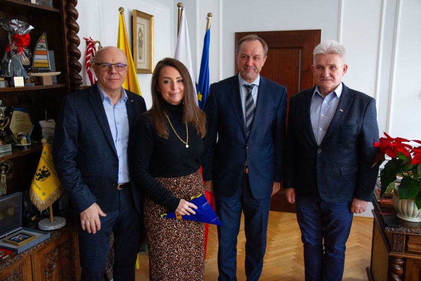 Cztery osoby w gabinecie. Kobieta trzyma flagę. W środku Marszałek Mieczysław Struk