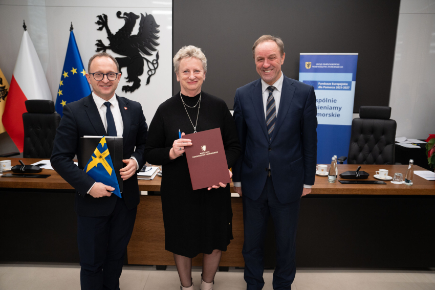 Marszałek Mieczysław Struk, wicemarszałek Marcin Skwierawski i jedna przedstawicielka władzy lokalnej prezentują podpisaną umowę i flagę Unii Europejskiej.