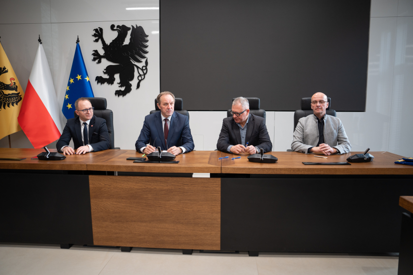 Cztery osoby przy biurku podpisują umowę