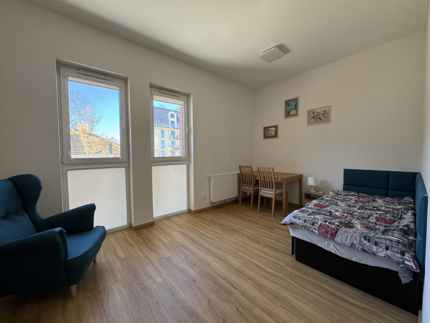 Pokój dla osoby z autyzmem w budynku. W ujęciu łóżko, stół z krzesłami i dwa okna