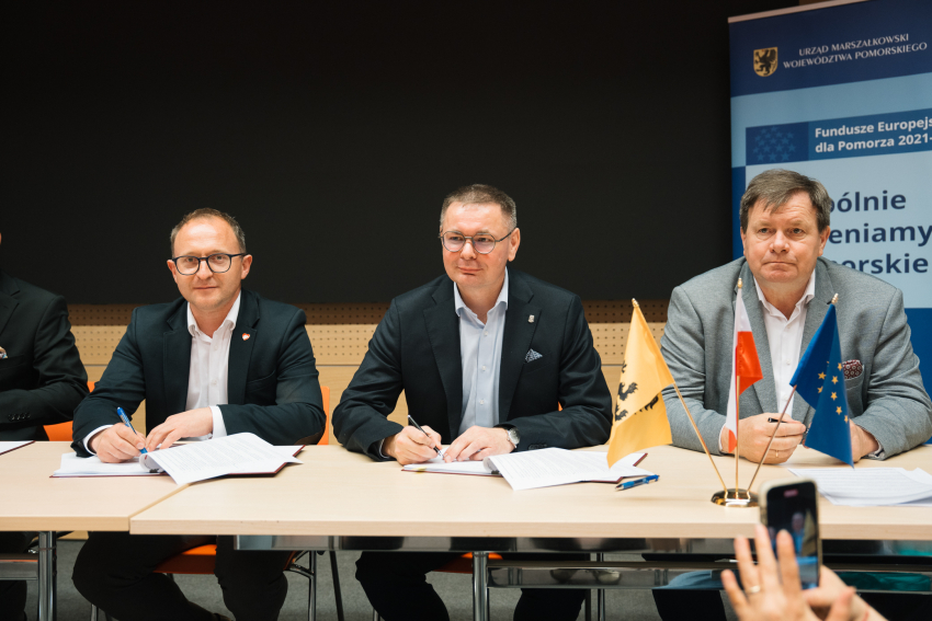 Zdjęcie: Łukasz Tokarczyk/Pomorskie.eu Zdjęcie przedstawia trzy osoby siedzące przy stole prezydialnym.