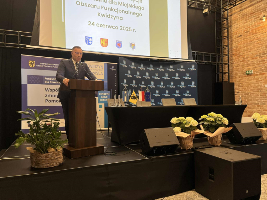 Zdjęcie przedstawia mężczyznę przy mównicy zabierającego głos.