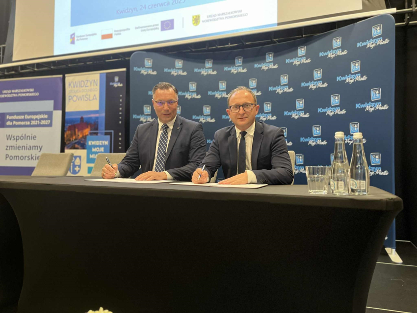 Zdjęcie przedstawia dwóch mężczyzn ubranych w garnitury przy stole prezydialnym.