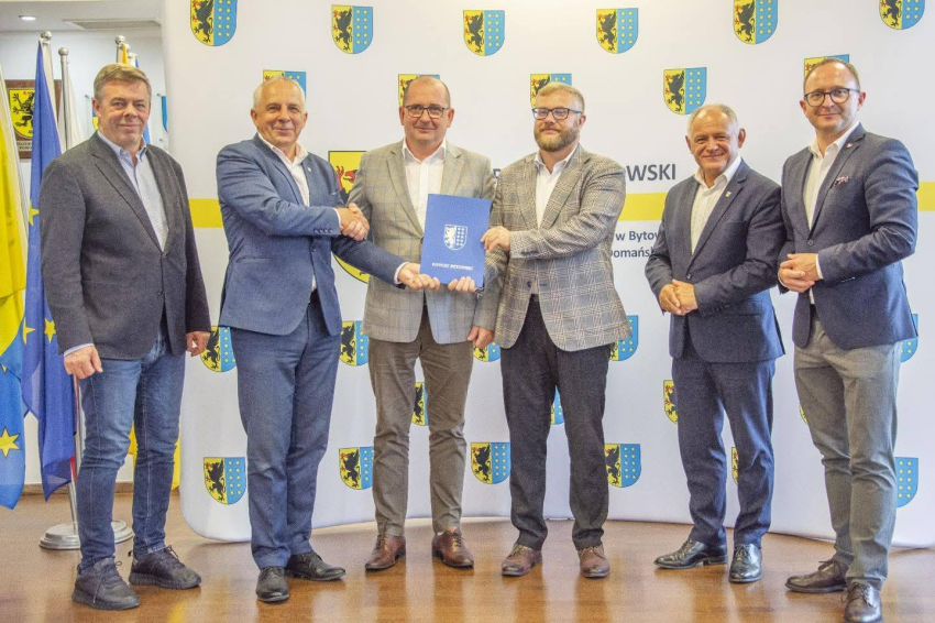 Sześć osób na zdjęciu. Osoby w środku trzymają teczkę z napisem powiat bytowski. Po prawej stornie zdjęcia Marszałek Marcin Skierawski