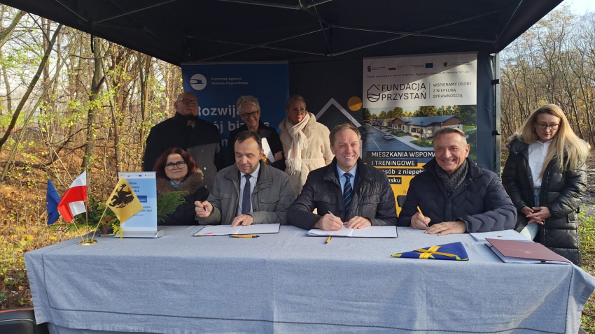 grupa ludzi przy stole. Podpisują uroczyście umowę o dofinansowanie