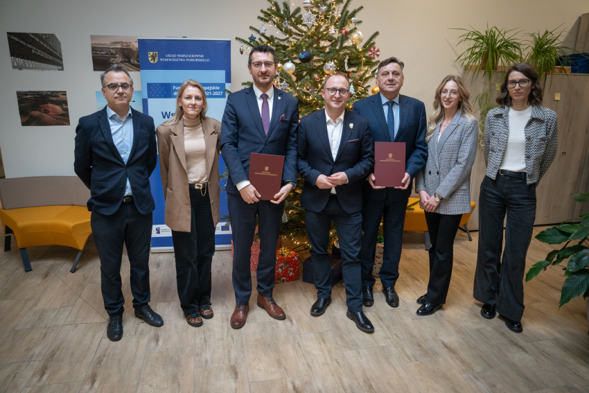 Siedem osób pozuje do zdjęcia i prezentuje podpisane porozumienia