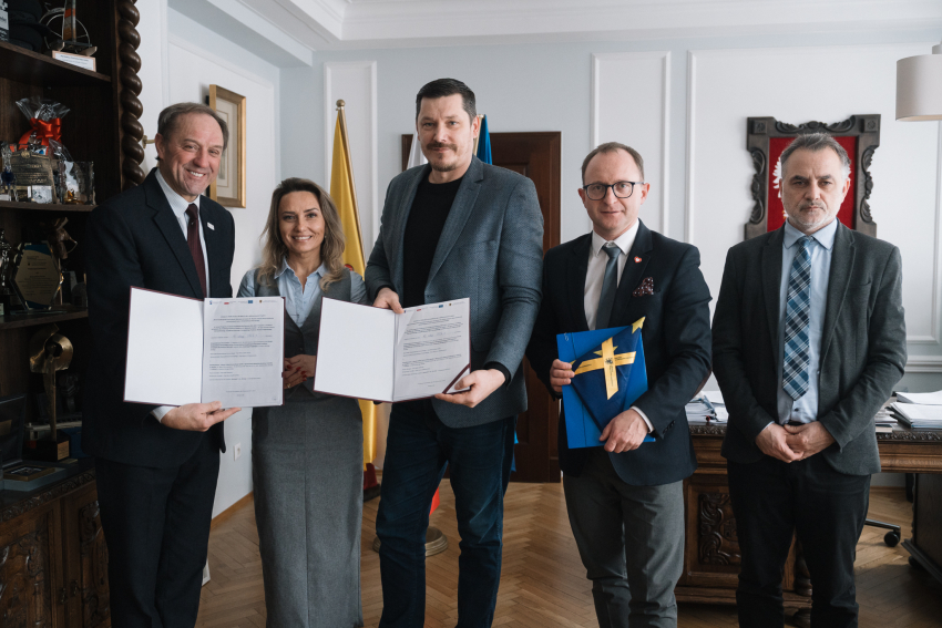 Od lewej: marszałek województwa pomorskiego Mieczysław Struk, przedstawicielka Miejskiego Zakładu Komunikacji w Słupsk oraz prezes tego zakładu, wicemarszałek Marcin Skwierawski oraz dyrektor Departamentu Programów Regionalnych Jan Szymański. Zebrane osoby pozują do uroczystego zdjęcia prezentując podpisane umowy oraz flagę Unii Europejskiej