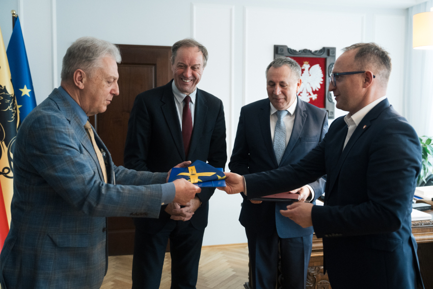 Dwóch wiceprezesów Copernicus Podmiot Leczniczy Sp. z o.o. oraz marszałek Mieczysław Struk i wicemarszałek Marcin Skwierawski pozują do zdjęcia i przekazują złożoną flagę UE gościom