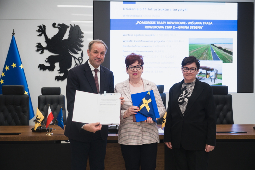 Marszałek Województwa Pomorskiego - Mieczysław Struk, wójt gminy Stegna oraz skarbnik gminy Stegna - Dorota Witkowska, pozują do uroczystego zdjęcia prezentując podpisaną umową o dofinansowanie i flagę Unii Europejskiej