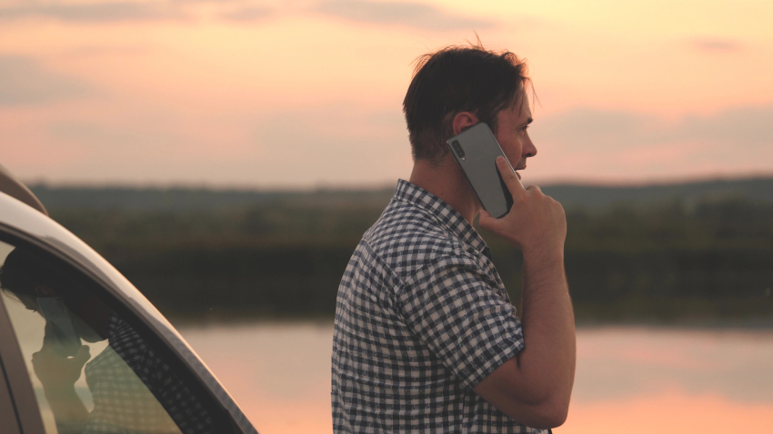 Mężczyzna z telefonem w ręku. W tle samochód