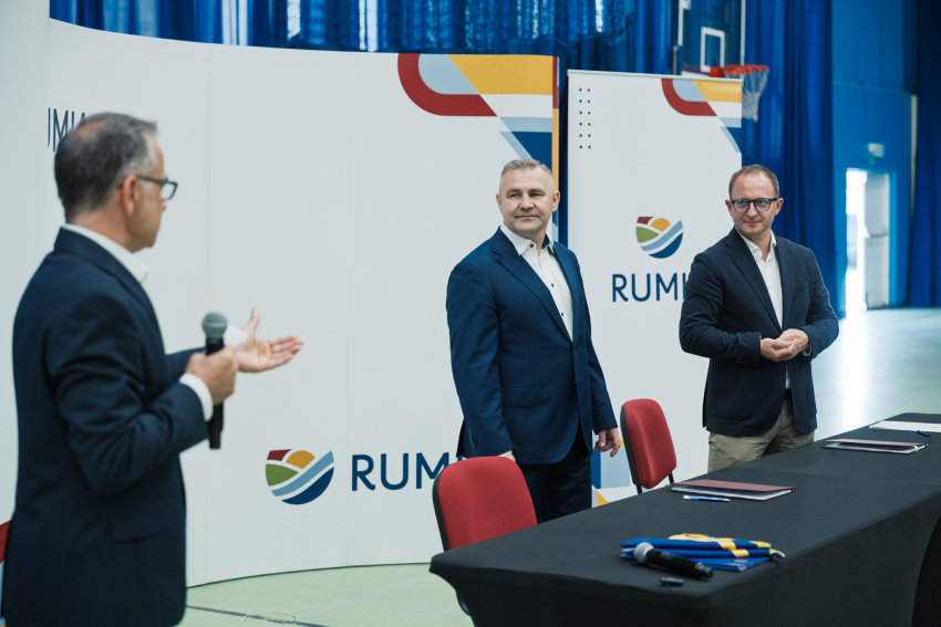 Burmistrz Rumi Michał Pasieczny oraz wicemarszałek województwa pomorskiego Marcin Skwierawski stoją przy stole prezydialnym. Spotkanie prowadzi i przemawia do zebranych Jan Szymański - dyrektor Departamentu Programów Regionalnych