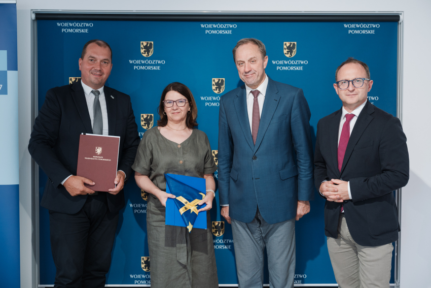Marszałek Mieczysław Struk, wicemarszałek Marcin Skwierawski, wójt gminy Szemud Ryszard Kalkowski oraz skarbnik gminy Szemud Teresa Pustelnik pozują do uroczystego zdjęcia prezentując podpisaną umowę oraz flagę UE