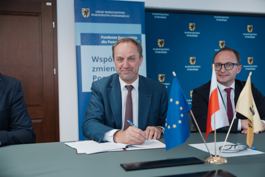 Marszałek Mieczysław Struk oraz wicemarszałek Marcin Skwierawski siedzą przy stole prezydialnym i podpisują umowę o dofinansowanie