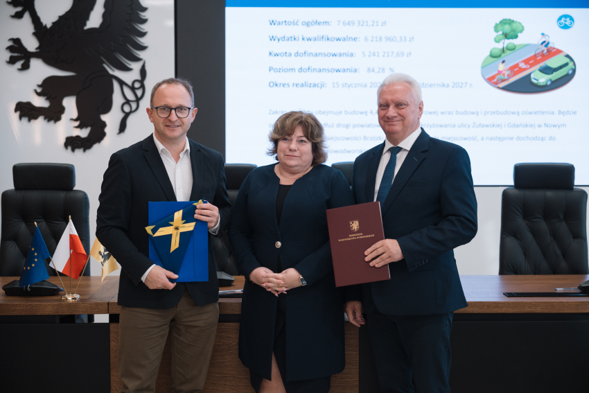 Wicemarszałek Marcin Skwierawski oraz dwóch przedstawicielki lokalnych władz pozują do uroczystego zdjęcia prezentując podpisane umowy o dofinansowanie oraz flagi UE