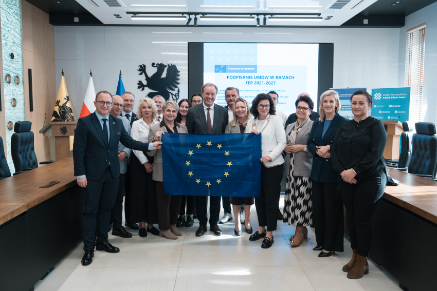 Siedemnaście osób pozuje do zdjęcia prezentując rozwiniętą flagę UE oraz podpisane umowy o dofinansowanie. Wśród tych osób jest marszałek woj. pomorskiego Mieczysław Struk i wicemarszałek Marcin Skwierawski