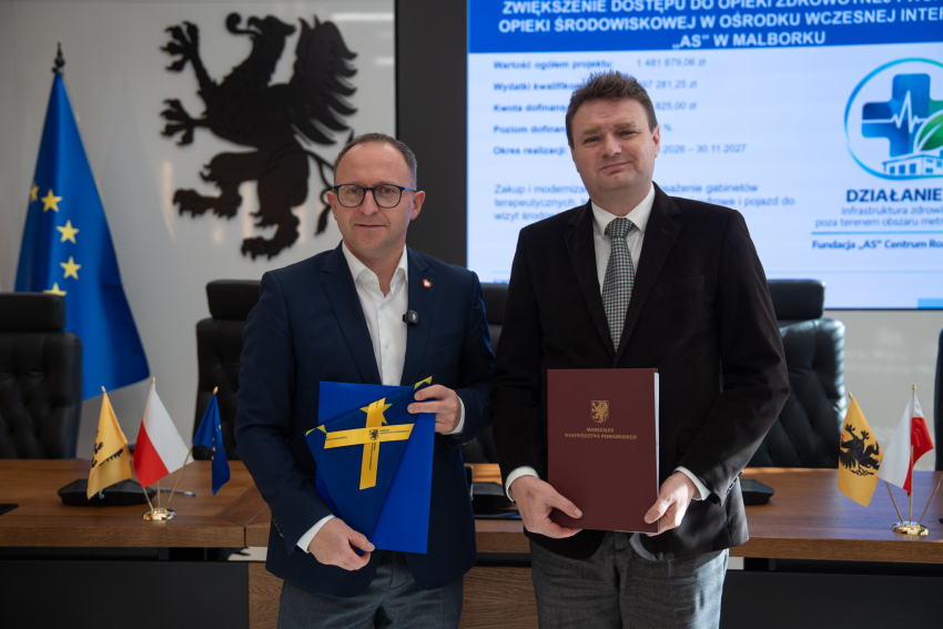 Wicemarszałek Marcin Skwierawski oraz przedstawiciel Fundacji "AS" Centrum Rozwoju Dzieci pozują do uroczystego zdjęcia prezentując podpisaną umowę o dofinansowanie oraz flagę UE