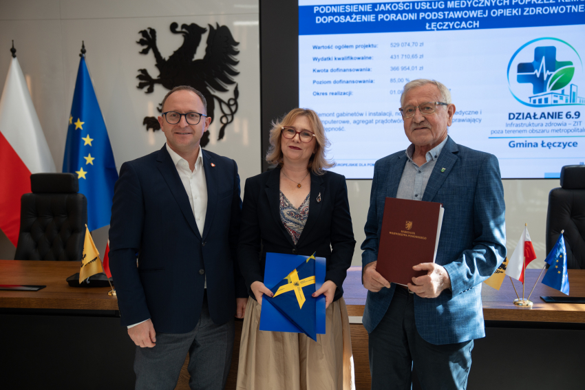 Wicemarszałek Marcin Skwierawski oraz dwuch przedstawicieli Gminy Łęczyce pozują do uroczystego zdjęcia prezentując podpisaną umowę o dofinansowanie oraz flagę UE