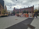 Wyremontowany plac wyłożony betonową kostką. Na środku placu trójwymiarowy napis &amp;quot;KONESER&amp;quot;, w tle grupa ludzi i wyremontowane kamienice z czerwonej cegły