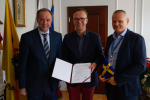 Cztery osoby w gabinecie. Mężczyzna w środku trzyma umowę. Po lewej stronie Marszałek Mieczysław Struk