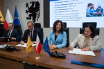 Cztery osoby siedzą przy stole prezydialnym i podpisują umowę