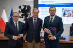 wicemarszałek Marcin Skwierawski, marszałek Mieczysław Struk oraz przedstawiciel władz regionu pozują do zdjęcia prezentując flagę i teczkę z dokumentem