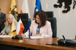 dwie osoby podpisują umowę o dofinansowanie przy stole prezydialnym