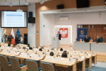 Sala, grupa osób słucha prelegenta