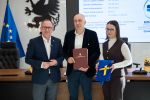 Wicemarszałek Marcin Skwierawski oraz dwóch przedstawicieli lokalnych władz pozują do uroczystego zdjęcia prezentując podpisaną umowę o dofinansowanie oraz flagę UE