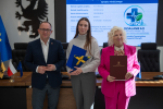 Wicemarszałek Marcin Skwierawski oraz dwie przedstawicielki Kwidzyńskiego Towarzystwa Przyjaciół Chorych pozują do uroczystego zdjęcia prezentując podpisaną umowę o dofinansowanie oraz flagę UE