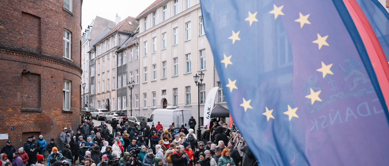 po prawej stronie unijna flaga, po lewej zwiedzający ludzie 