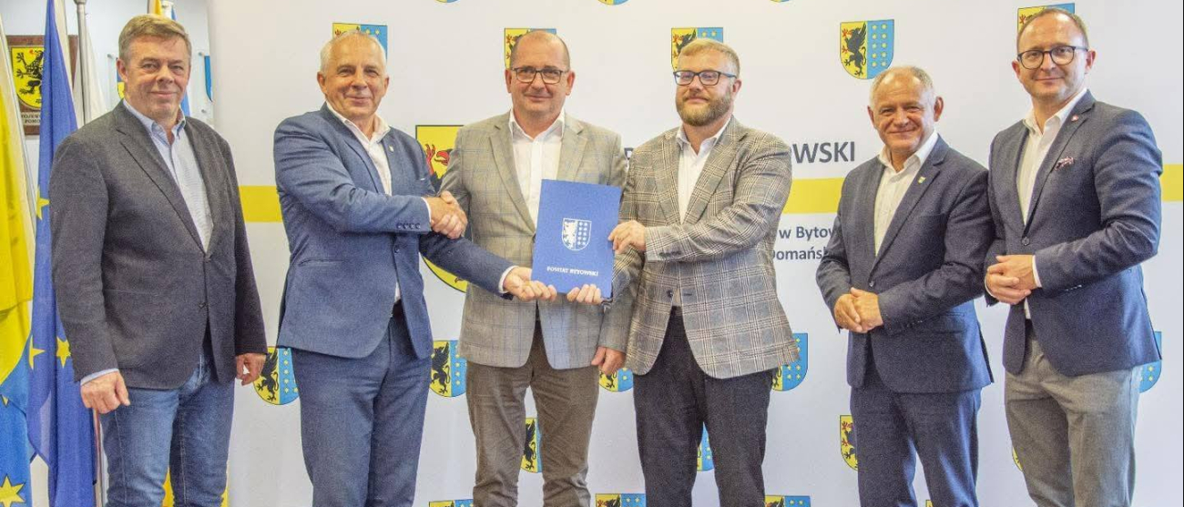 Sześć osób na zdjęciu. Osoby w środku trzymają teczkę z napisem powiat bytowski. Po prawej stornie zdjęcia Marszałek Marcin Skierawski