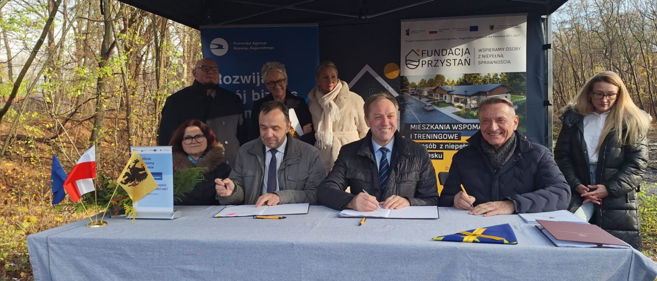 grupa ludzi przy stole. Podpisują uroczyście umowę o dofinansowanie