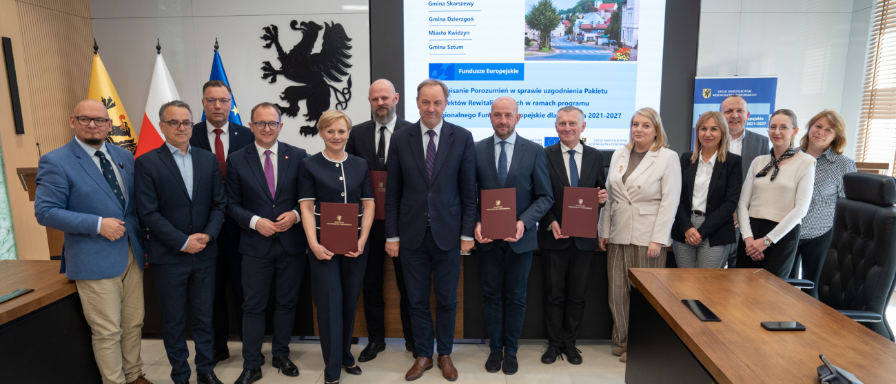 Czternaście osób pozuje do zdjęcia prezentując podpisane umowy. Wśród nich marszałek Mieczysław Struk, pracownicy urzędu marszałkowskiego oraz przedstawiciele lokalnych władz