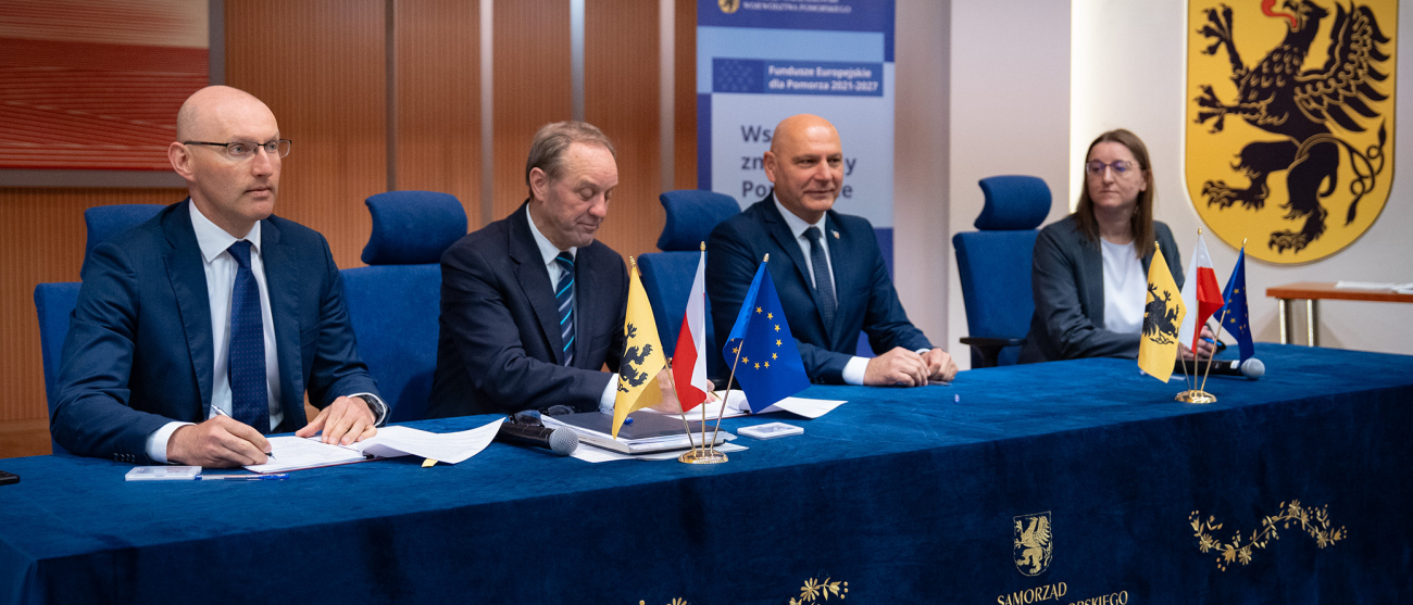 cztery osoby siedzą przy stole. Jedna z osób podpisuje dokument