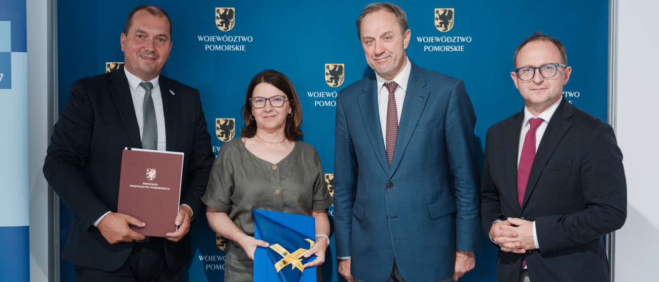 Marszałek Mieczysław Struk, wicemarszałek Marcin Skwierawski, wójt gminy Szemud Ryszard Kalkowski oraz skarbnik gminy Szemud Teresa Pustelnik pozują do uroczystego zdjęcia prezentując podpisaną umowę oraz flagę UE