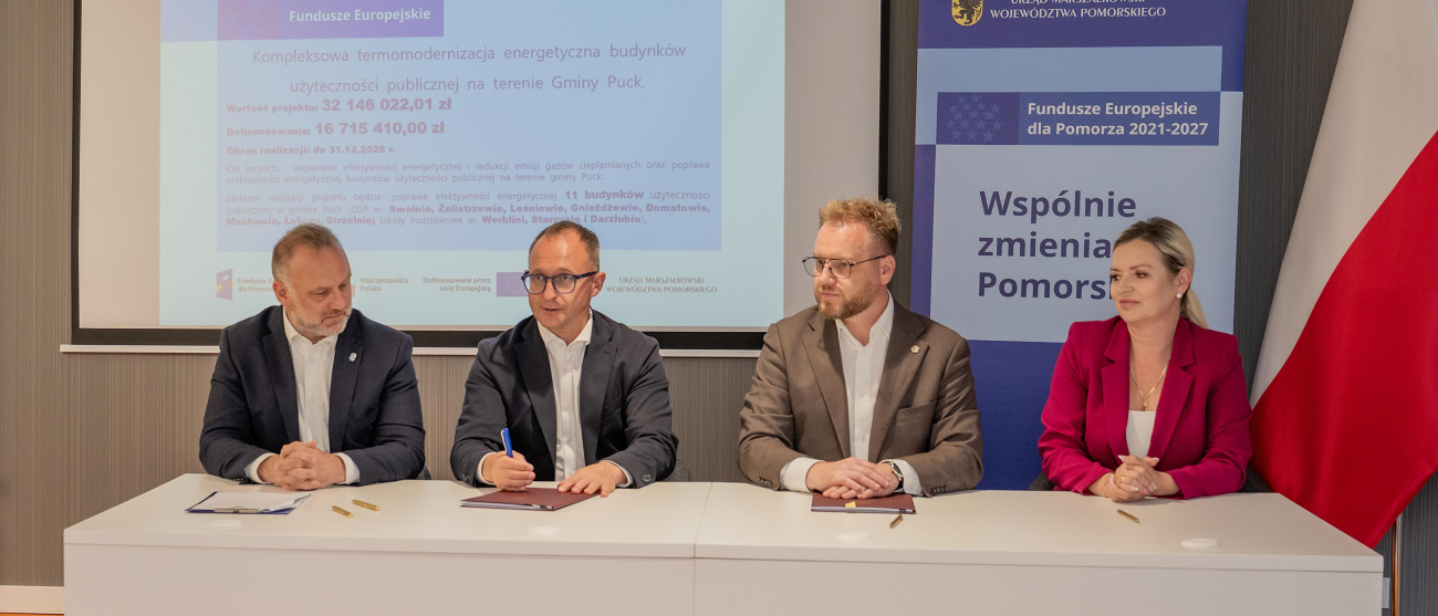 wicemarszałek Marcin Skwierawski oraz trzy inne osoby siedzą przy stole prezydialnym i podpisują umowę o dofinansowanie