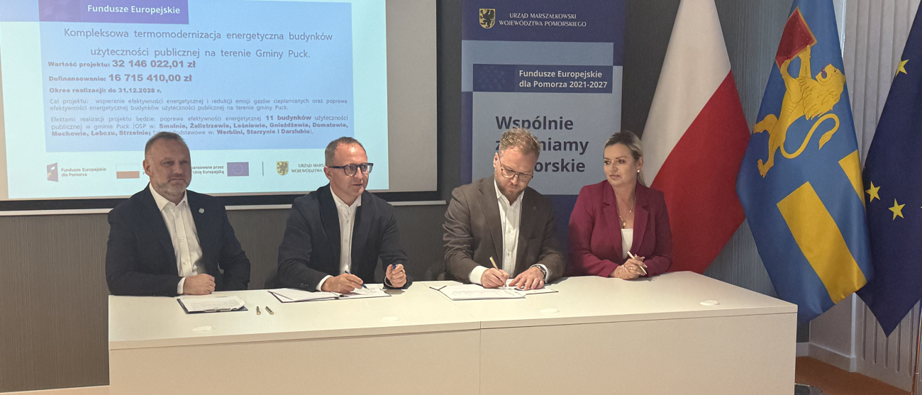 wicemarszałek Marcin Skwierawski oraz trzy inne osoby siedzą przy stole prezydialnym i podpisują umowę o dofinansowanie