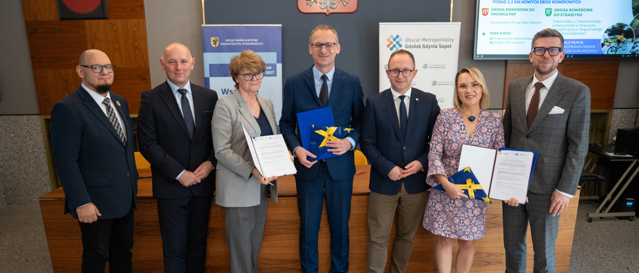 Siedem osób prezentuje podpisane umowy. Od lewej: Marcin Fuchs - dyrektor Departamentu Europejskiego Funduszu Społecznego urzędu marszałkowskiego, Radosław Pietrzak - Zastępca Burmistrza Pruszcza Gdańskiego ds. Komunalnych, Maria Niderla - Skarbnik Pruszcza Gdańskiego, Janusz Wróbel – Burmistrz Pruszcza Gdańskiego, Marcin Skwierawski – Wicemarszałek Województwa Pomorskiego, Weronika Chmielowiec – Wójt Gminy Pruszcz Gdański, Michał Glaser – prezes Zarządu Obszar Metropolitalny Gdańsk-Gdynia-Sopot